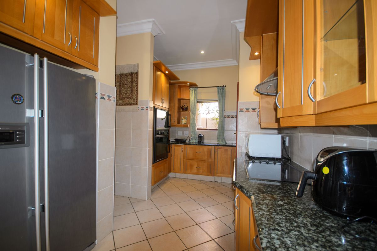 A functional kitchen featuring wooden cabinetry, granite countertops, built-in oven, extractor fan, and tiled flooring with a neutral backsplash.