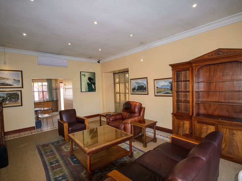 Spacious living room featuring tiled flooring, recessed downlighting, crown molding, and a wall-mounted air conditioning unit, with an open transition to the kitchen area.