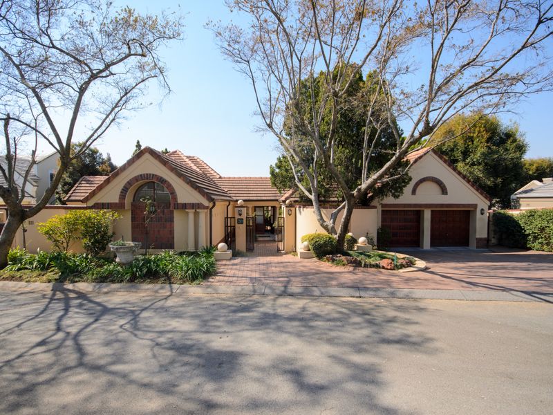 Front elevation of a single-story house featuring a paved driveway, double garage, and an arched entrance with a gated courtyard.