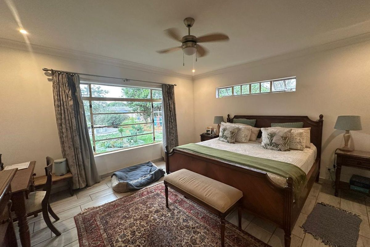 Spacious bedroom featuring tiled flooring, a ceiling fan, and large windows providing natural light and garden views.