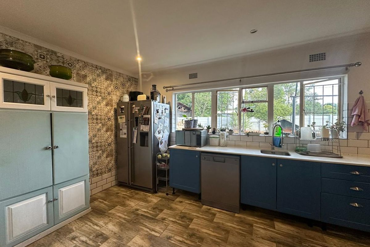 A functional kitchen featuring blue cabinetry, a stainless steel sink, patterned feature wall, and tiled flooring with ample natural light.