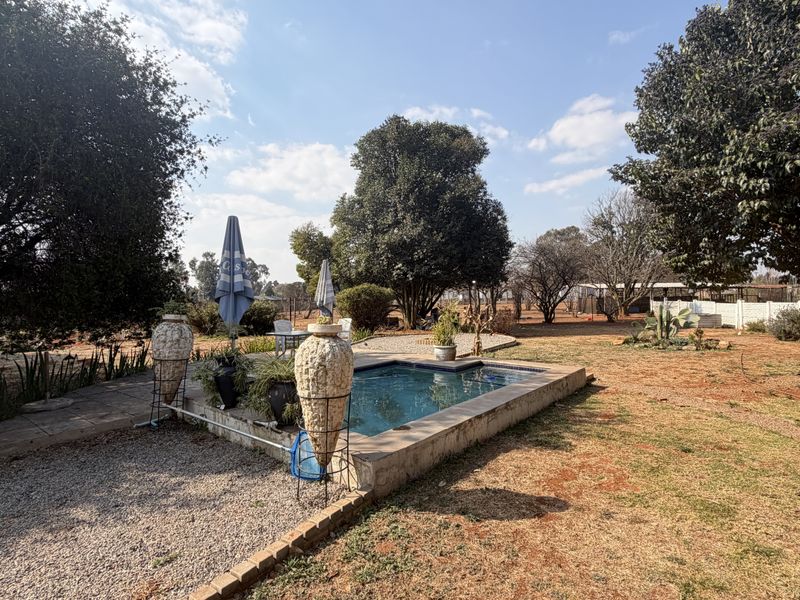 Outdoor pool area featuring a small swimming pool set within a gravel and paved garden space on a small holding property.