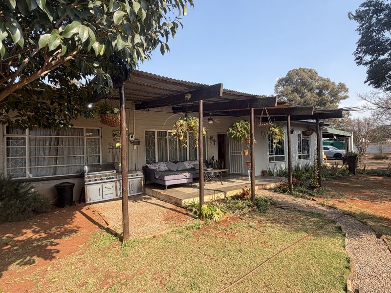 A covered outdoor patio area featuring a corrugated iron roof and timber support beams, overlooking a spacious garden setting.