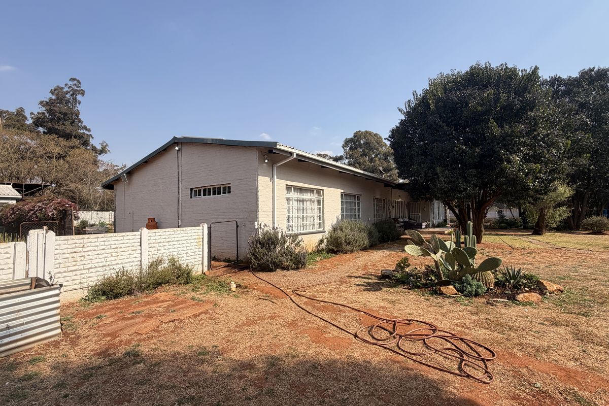 Rear view of the property showing the main dwelling, brick exterior, security features, and surrounding garden area with established trees.