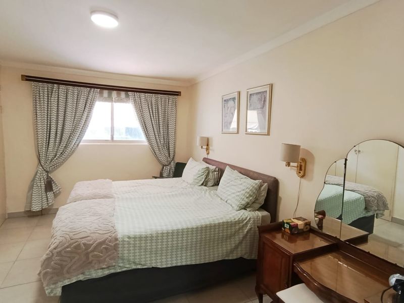A well-lit bedroom featuring built-in cupboards, tiled flooring, and wall-mounted lighting, offering a functional and comfortable living space.