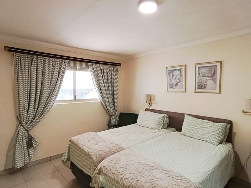 A functional bedroom featuring tiled flooring, wall-mounted lighting fixtures, and a window with curtain treatments.