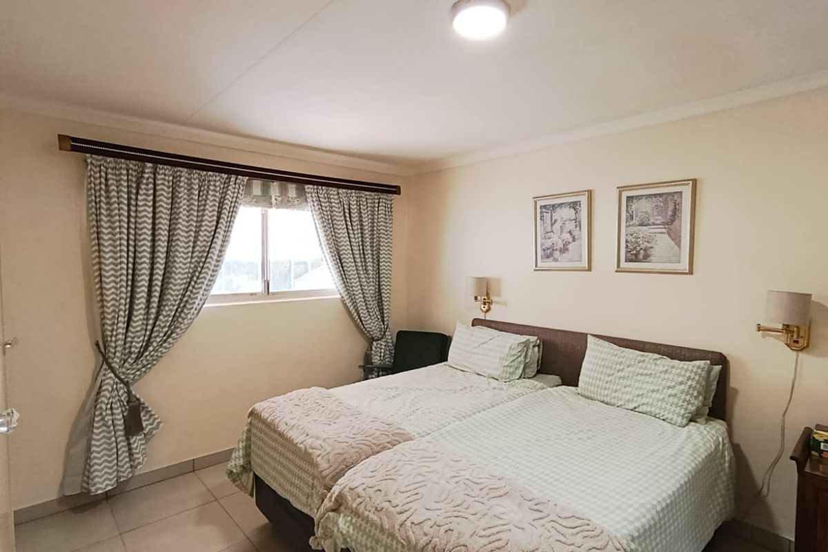 A functional bedroom featuring tiled flooring, wall-mounted lighting fixtures, and a window with curtain treatments.