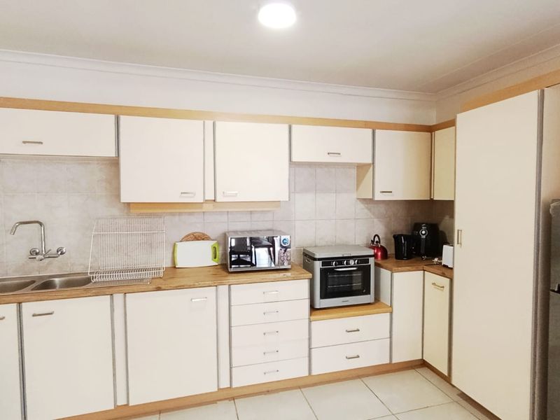 A functional kitchen featuring light-toned cabinetry, laminate countertops, a double bowl sink, tiled splashback, and a built-in oven with tiled flooring.
