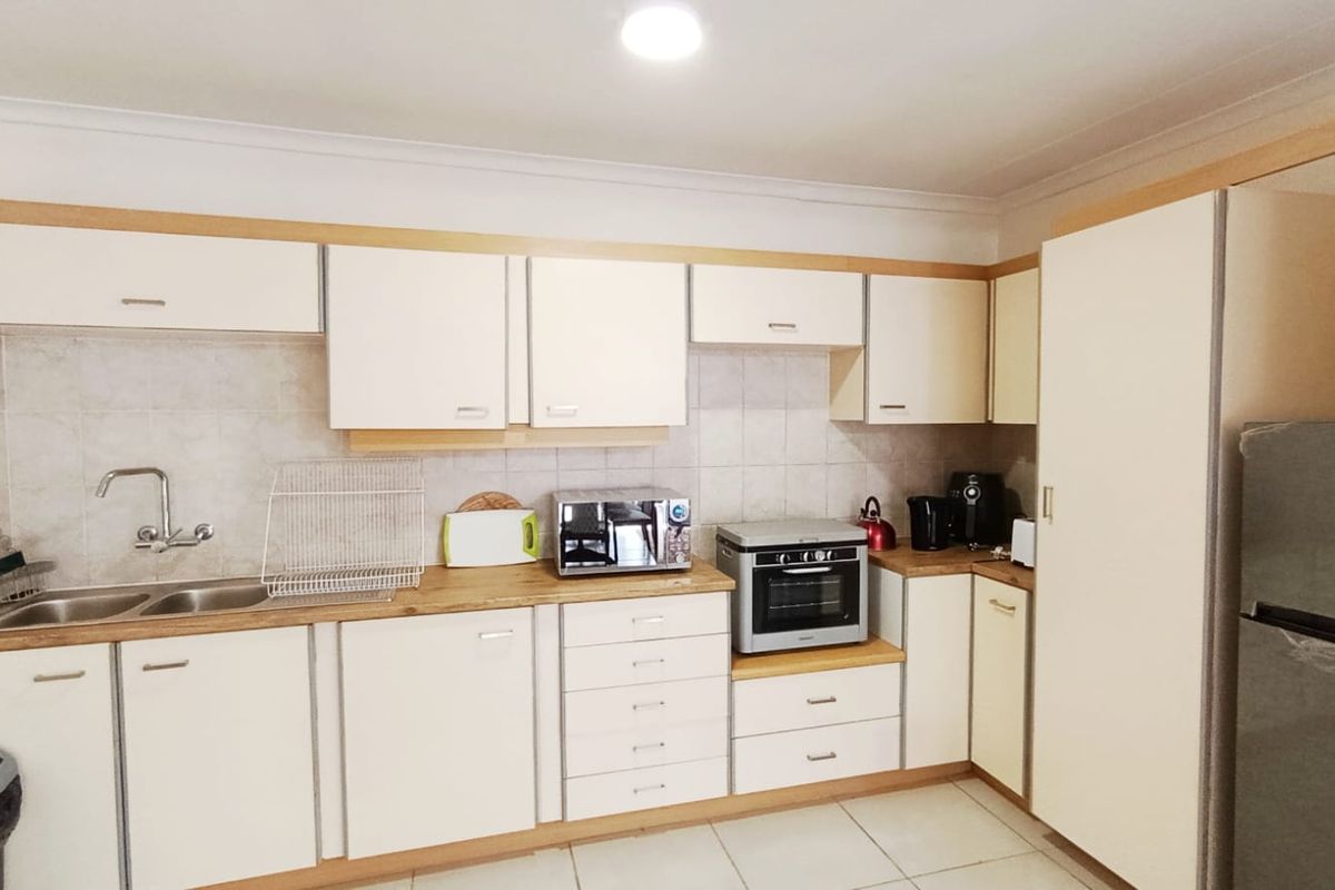 A functional kitchen featuring light-toned cabinetry, laminate countertops, a double bowl sink, tiled splashback, and a built-in oven with tiled flooring.
