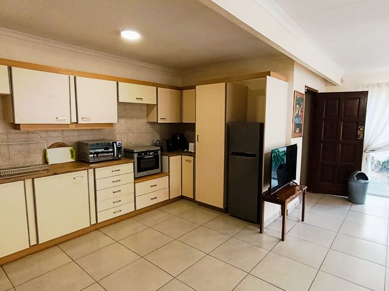 Open-plan kitchen area featuring neutral built-in cabinetry, tiled flooring, and direct access to the exterior through a solid timber door.