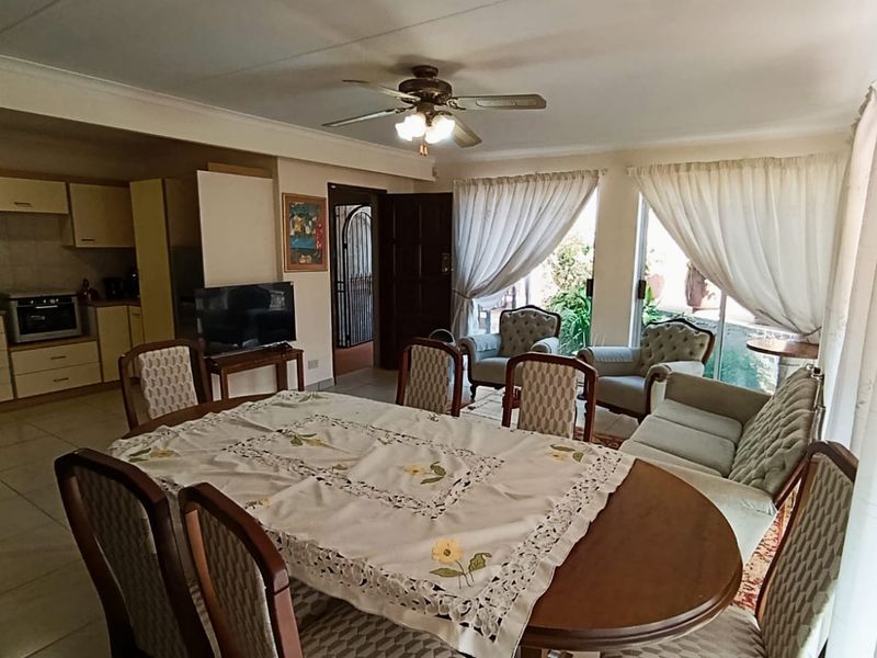 Open-plan living and dining area featuring tiled floors, a ceiling fan, and an integrated kitchen with built-in cabinetry and appliances.