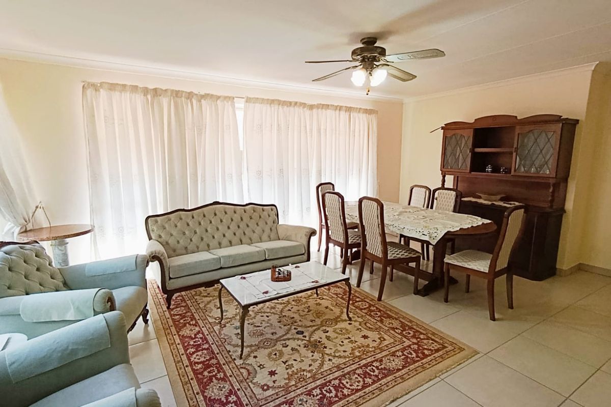 Spacious open-plan living and dining area featuring neutral tiled flooring, coved cornicing, and a central ceiling fan.