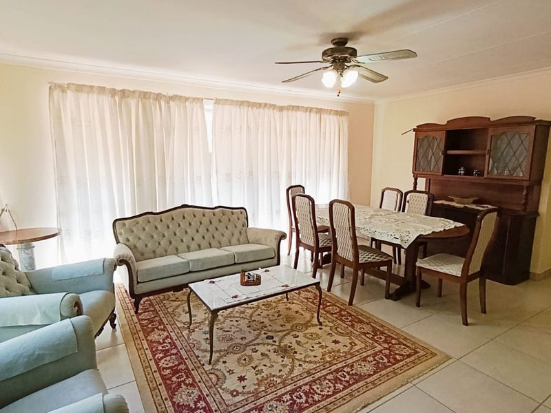 Spacious open-plan living and dining area featuring neutral tiled flooring, coved cornicing, and a central ceiling fan.