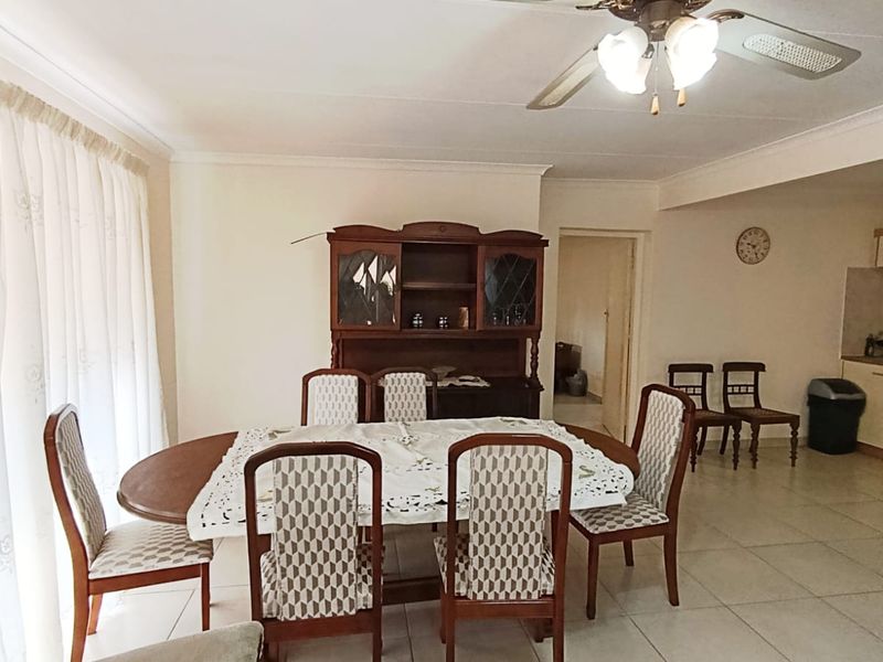 Open plan living and dining area featuring tiled flooring, a ceiling fan, and an adjoining kitchen with built-in cabinetry.