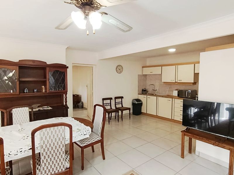 Open-plan living and dining area featuring tiled flooring, a ceiling fan, and a functional kitchen with built-in cabinetry and sink.
