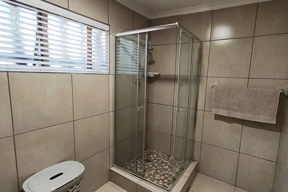 A clean, functional bathroom featuring a glass-enclosed shower with a pebble-tiled floor and neutral ceramic wall tiling throughout.