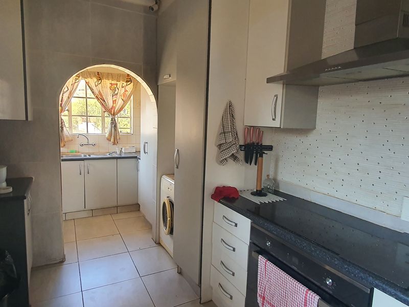 Functional kitchen featuring built-in cabinetry, integrated oven and hob, extractor fan, and a separate scullery area accessible through an arched doorway.