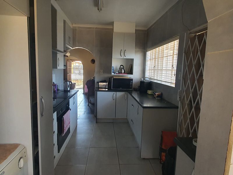 Functional kitchen featuring built-in cabinetry, laminate countertops, and tiled flooring, with an open archway leading to the adjacent living area.
