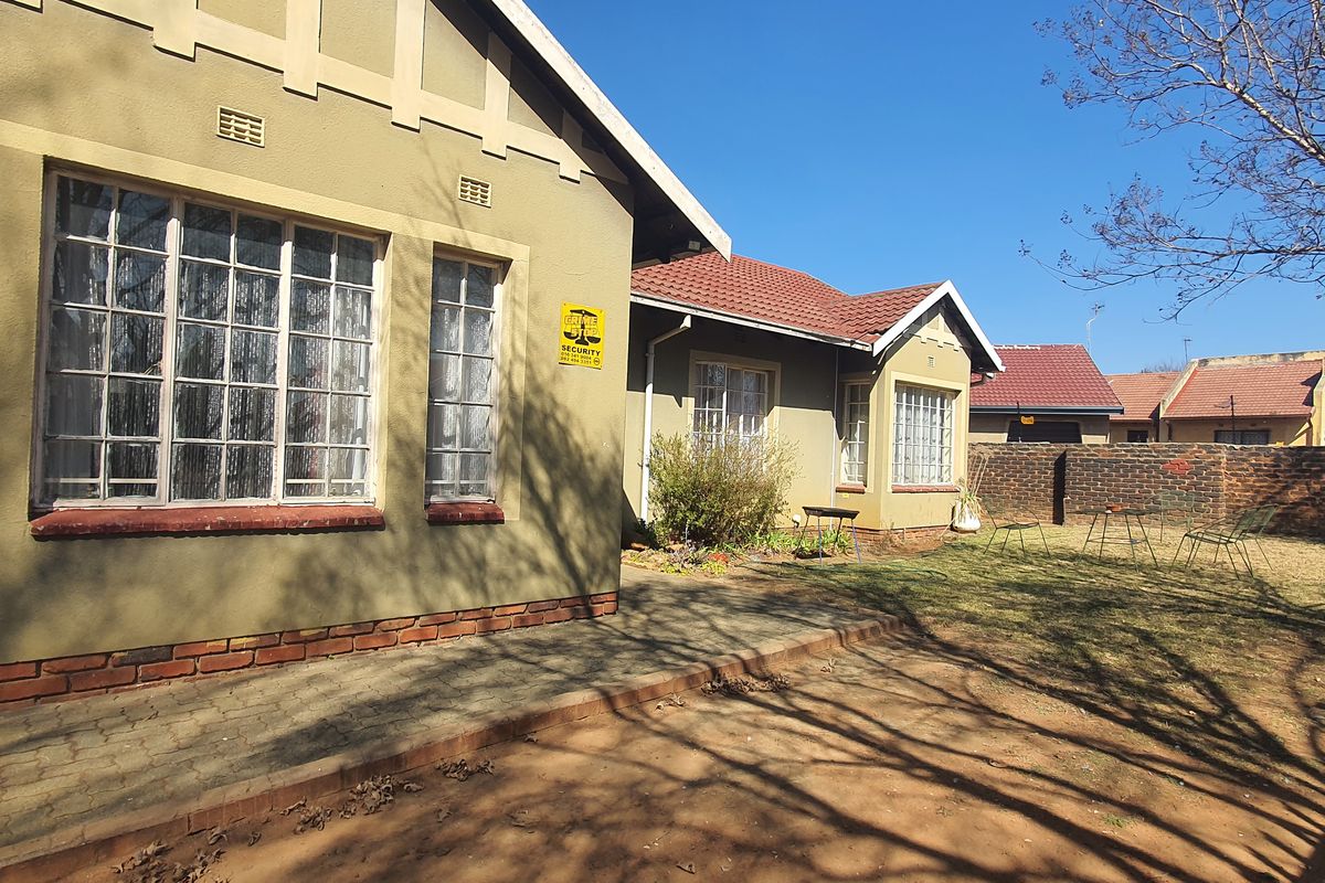 Rear view of the house featuring a paved patio area, brick boundary wall, and a garden space with established trees.