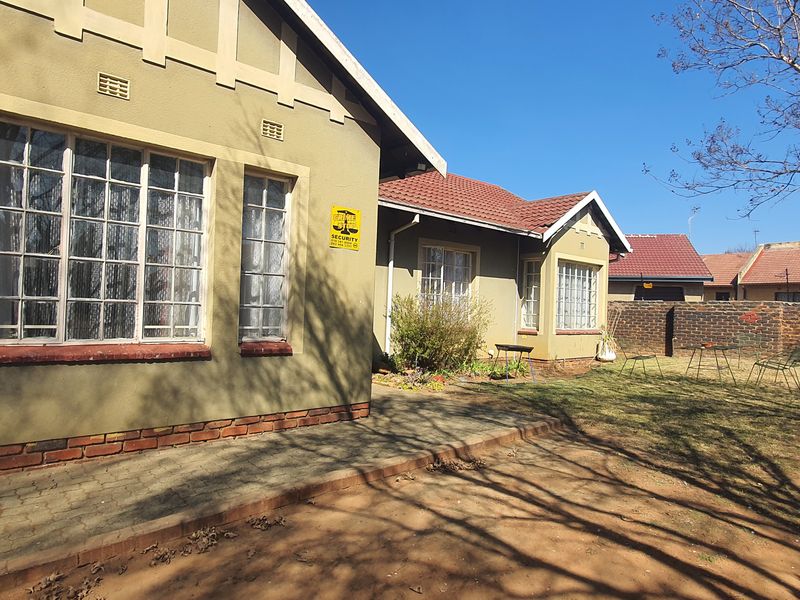 Rear view of the house featuring a paved patio area, brick boundary wall, and a garden space with established trees.