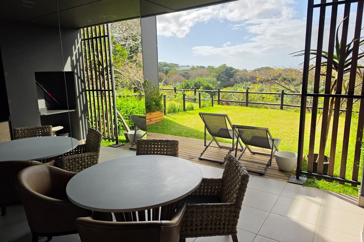 Covered patio featuring a built-in braai, tiled flooring, and timber decking, opening onto a private garden with scenic views.