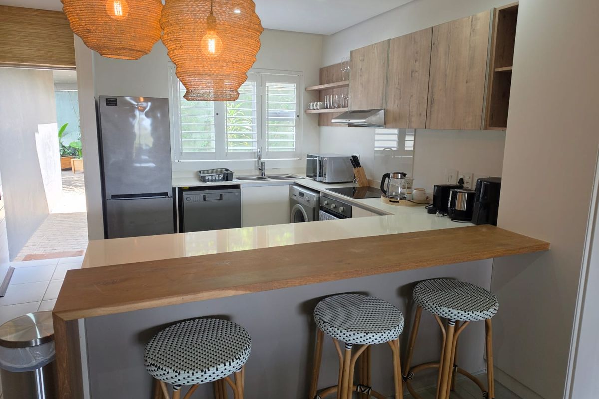 Modern kitchen featuring wood-tone cabinetry, stone countertops, a breakfast bar, and integrated appliances, with direct access to an outdoor patio area.