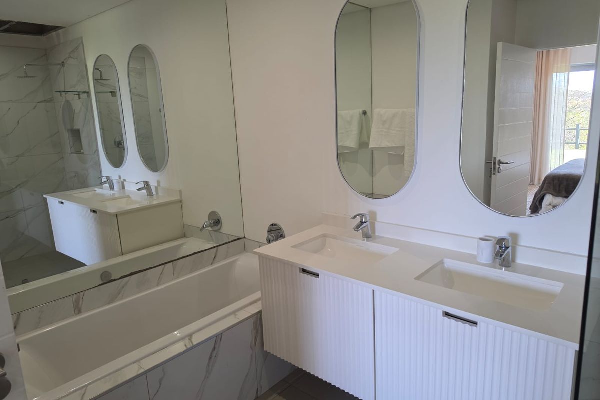Modern bathroom featuring a double vanity with white fluted cabinetry, marble-look tiling, a built-in bathtub, and a separate shower area.
