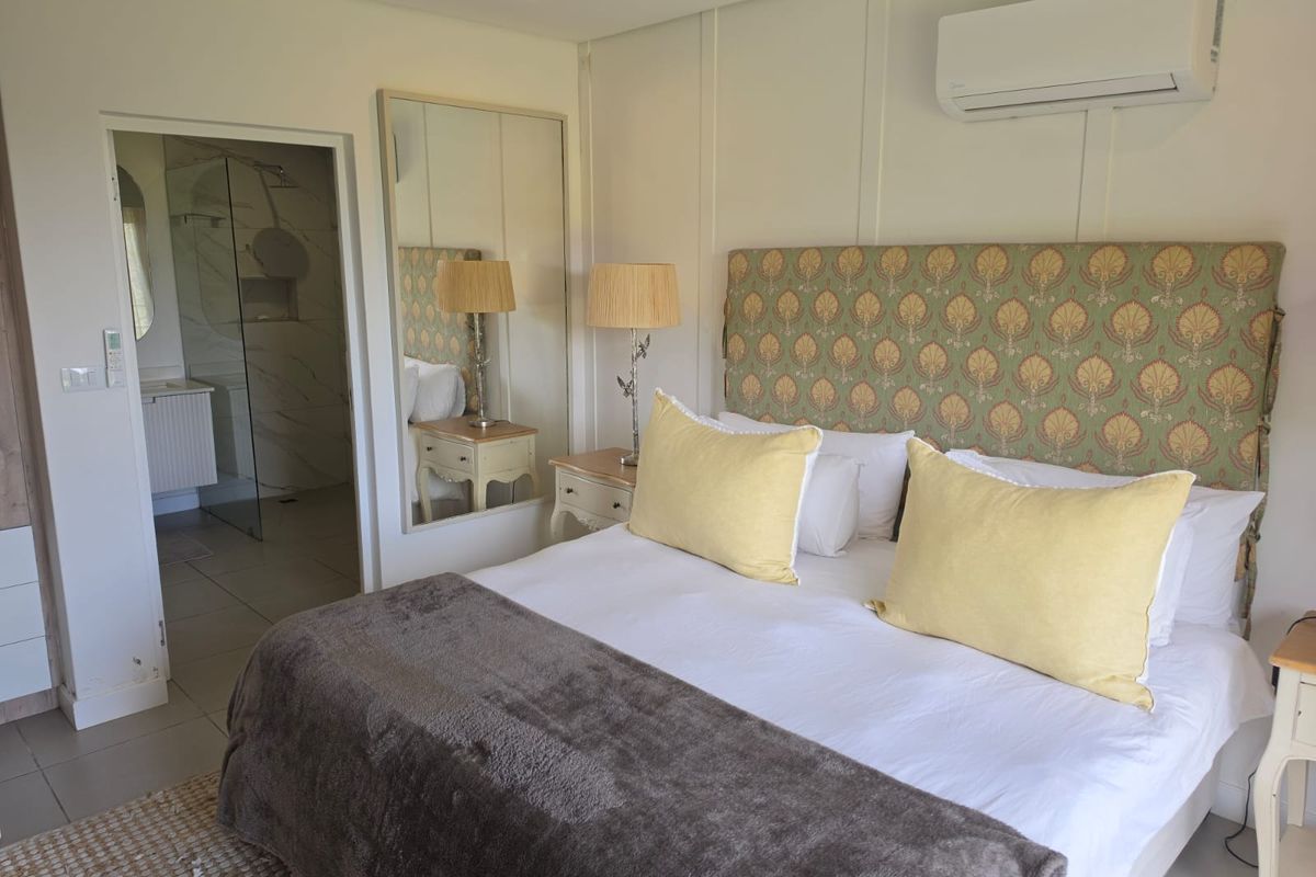 A well-maintained bedroom featuring a neutral palette, wall-mounted air conditioning, recessed lighting, and direct access to an en-suite bathroom.