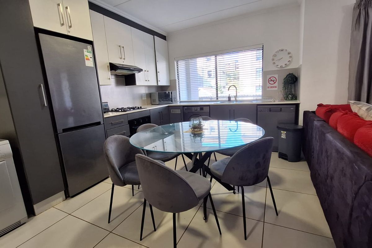 Open-plan kitchen and dining area featuring modern two-tone cabinetry, gas hob, and tiled flooring, seamlessly integrated with the living space.