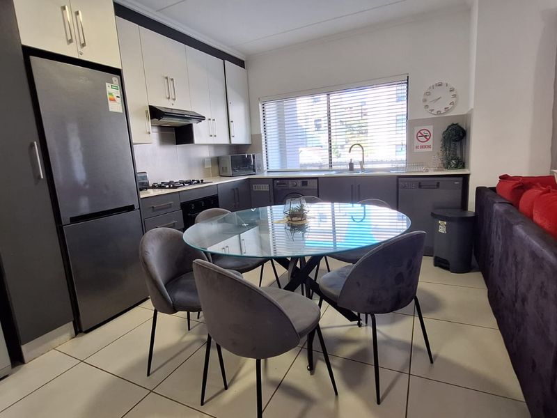 Open-plan kitchen and dining area featuring modern two-tone cabinetry, gas hob, and tiled flooring, seamlessly integrated with the living space.