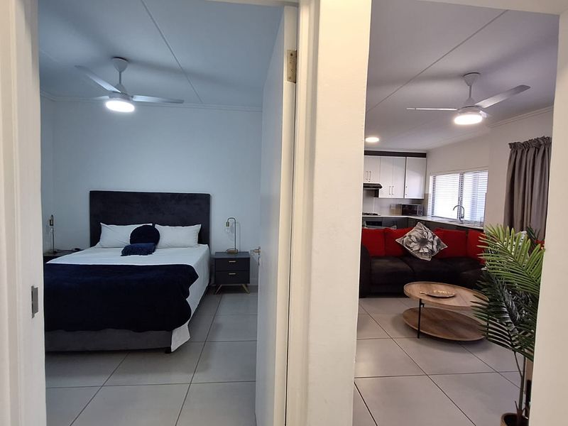 A view through a doorway showing a bedroom on the left and an open-plan kitchen and living area on the right.