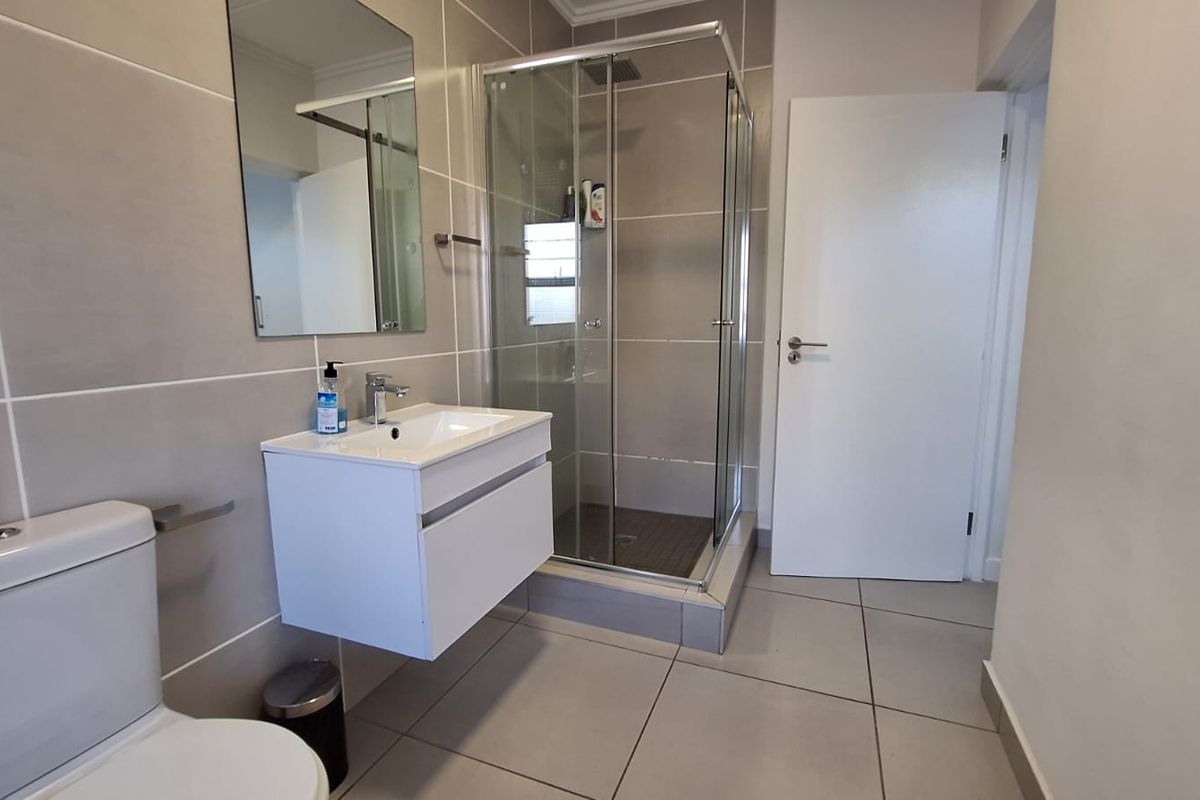 Modern bathroom featuring a wall-mounted vanity, glass shower enclosure, and neutral ceramic tiling throughout.