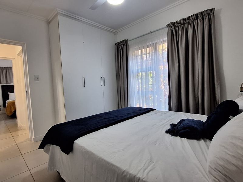 A well-maintained bedroom featuring built-in cupboards, tiled flooring, and a ceiling fan, with an adjoining hallway view.