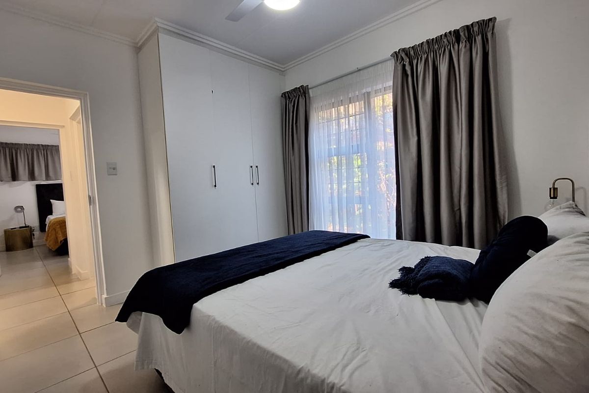 A well-maintained bedroom featuring built-in cupboards, tiled flooring, and a ceiling fan, with an adjoining hallway view.