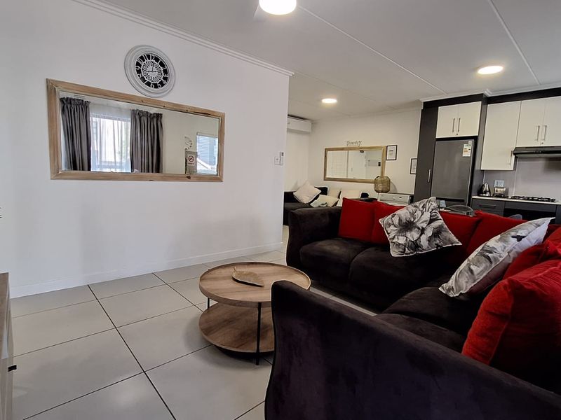 An open-plan living and kitchen area featuring modern tiled flooring, neutral cabinetry, and integrated kitchen appliances, creating a functional and cohesive living space.