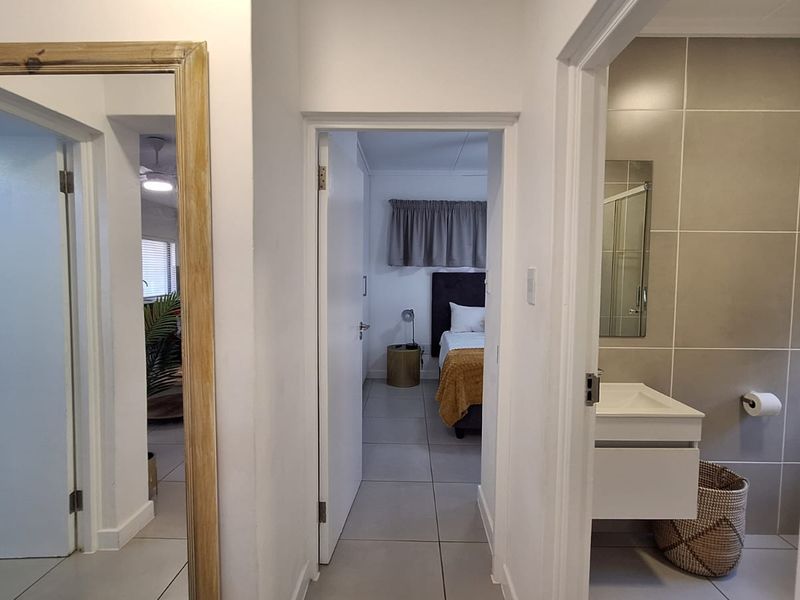 A bright hallway connecting to a bedroom and a modern bathroom featuring a wall-mounted vanity and large format tiling.