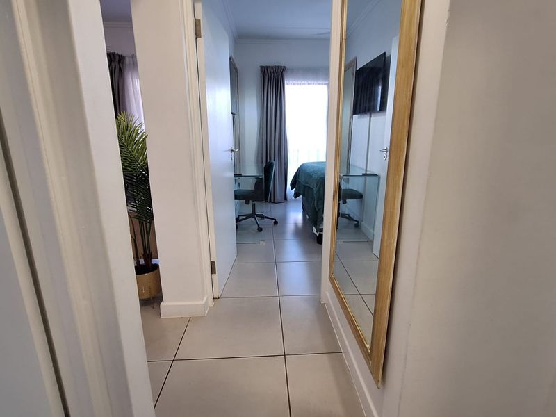 A bright hallway with neutral tiled flooring providing access to adjacent rooms, featuring clean lines and a functional layout.