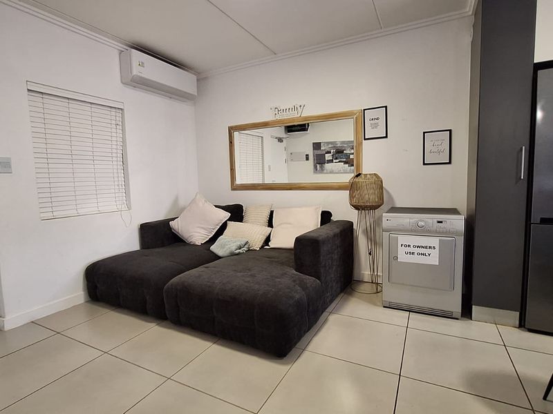 An open-plan living area featuring tiled flooring, a wall-mounted air conditioning unit, and neutral finishes, providing a functional and versatile space.
