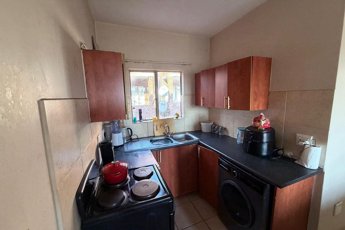 Compact kitchen featuring laminate cabinetry, dark countertops, tiled backsplash, and integrated laundry facilities, offering a functional layout for an apartment.