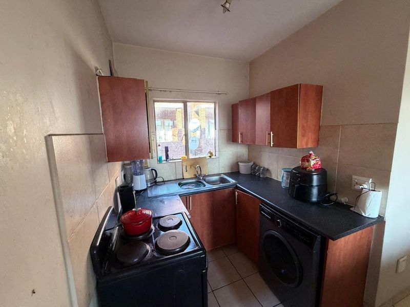 Compact kitchen featuring laminate cabinetry, dark countertops, tiled backsplash, and integrated laundry facilities, offering a functional layout for an apartment.