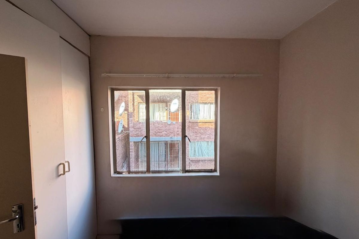 A compact bedroom featuring a built-in wardrobe and a metal-framed window, offering a functional space ready for modernization and personal styling.