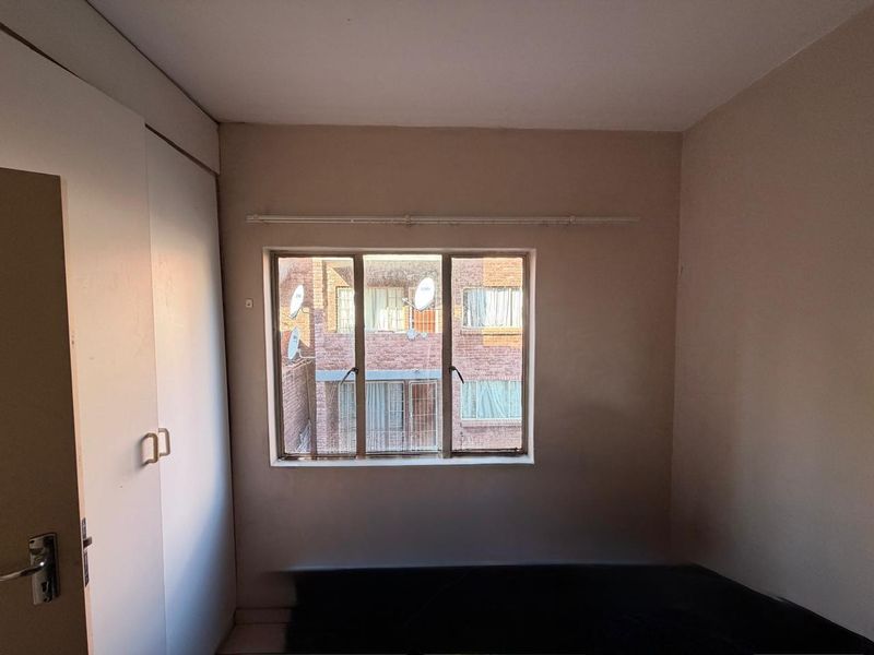 A compact bedroom featuring a built-in wardrobe and a metal-framed window, offering a functional space ready for modernization and personal styling.