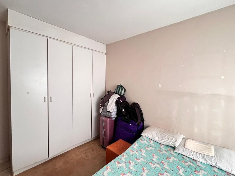 A bedroom featuring a large built-in wardrobe with white doors and carpeted flooring, requiring minor cosmetic updates to the wall finishes.