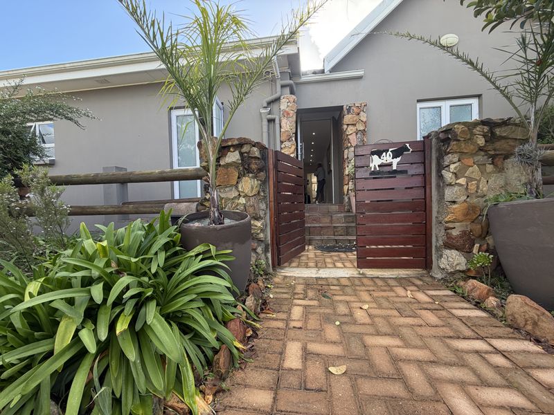 Front entrance view featuring a brick paved walkway, stone-clad pillars, and a timber gate leading to the main house entrance.