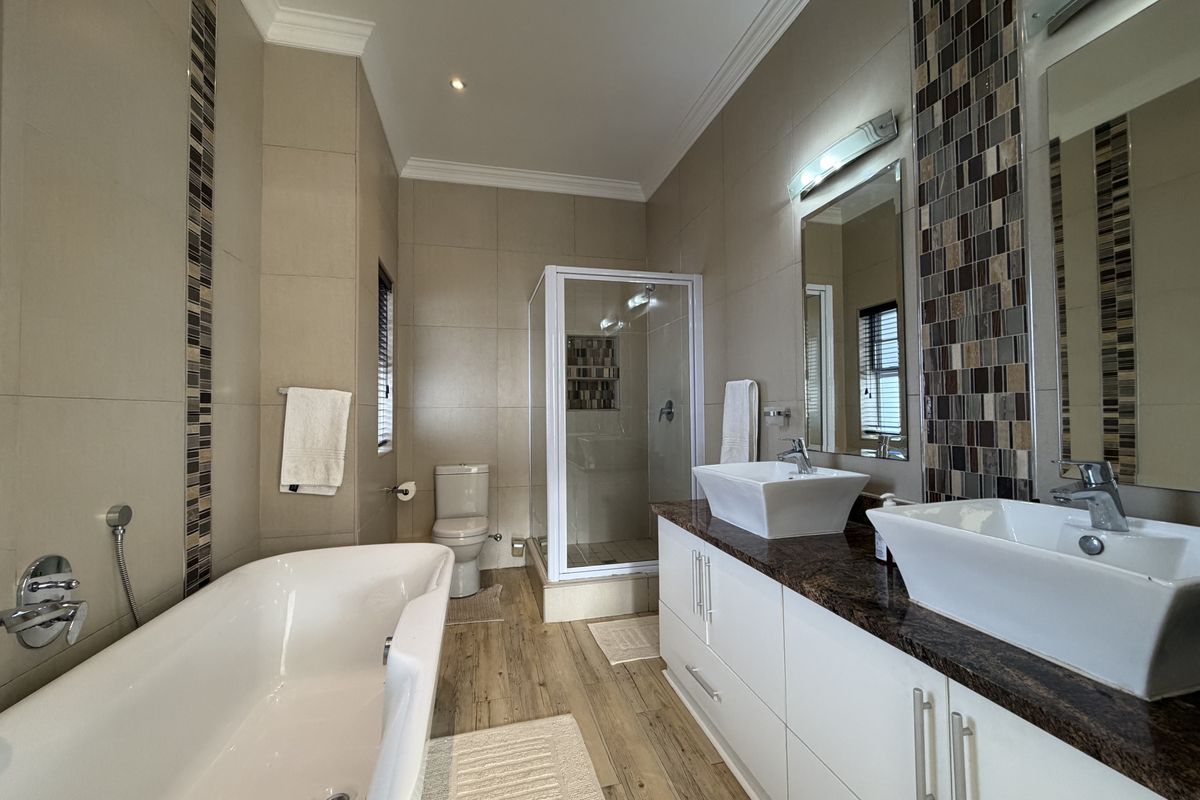 Modern bathroom featuring a freestanding bathtub, double vanity with vessel sinks, granite countertops, and a separate glass-enclosed shower with mosaic tile detailing.