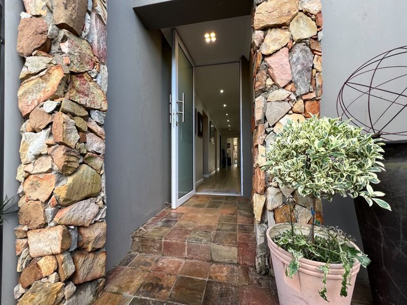 Inviting entrance featuring natural stone cladding pillars, tiled steps, and a modern pivot door leading into the home's interior hallway.