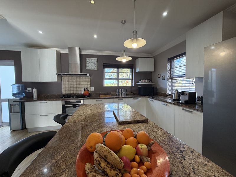 A well-appointed kitchen featuring granite countertops, a central island, built-in oven, gas hob, and modern cabinetry with recessed and pendant lighting.