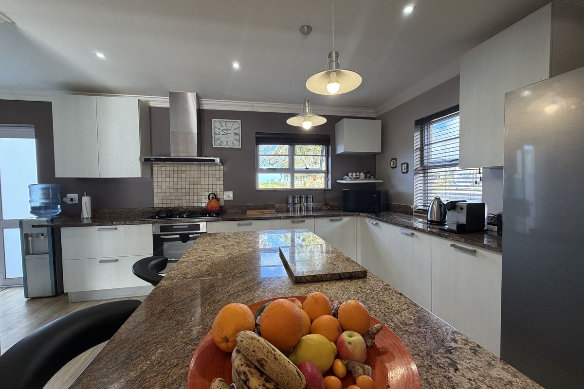 A well-appointed kitchen featuring granite countertops, a central island, built-in oven, gas hob, and modern cabinetry with recessed and pendant lighting.