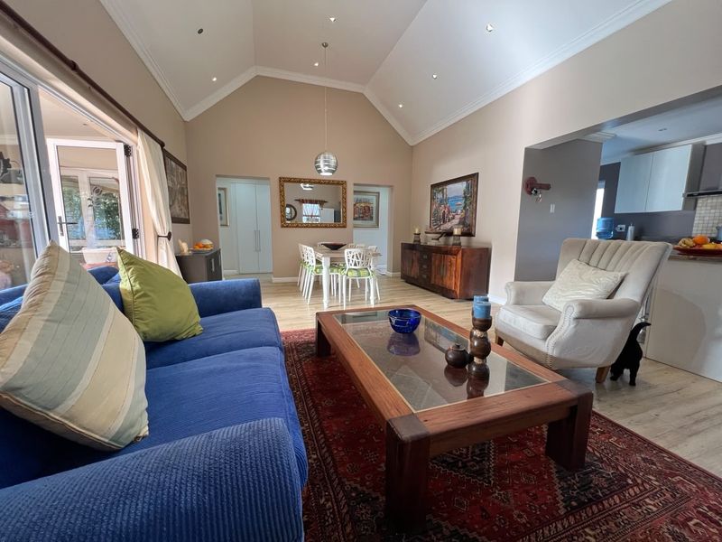 Spacious open-plan living and dining area featuring a high vaulted ceiling, recessed lighting, and seamless flow to the outdoor patio through sliding glass doors.