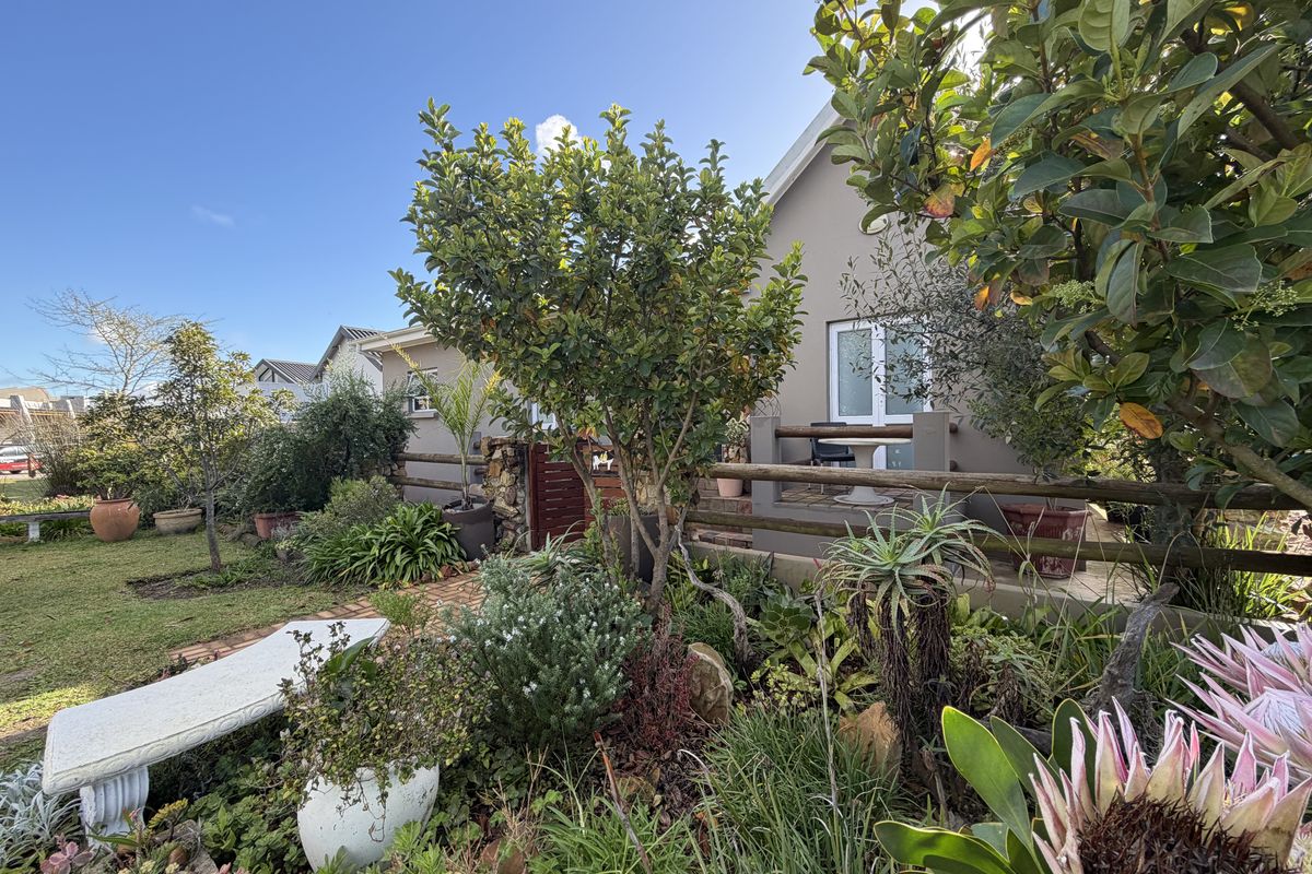 A well-maintained rear garden featuring a brick pathway, established landscaping, and a covered patio area accessible via a sliding glass door.